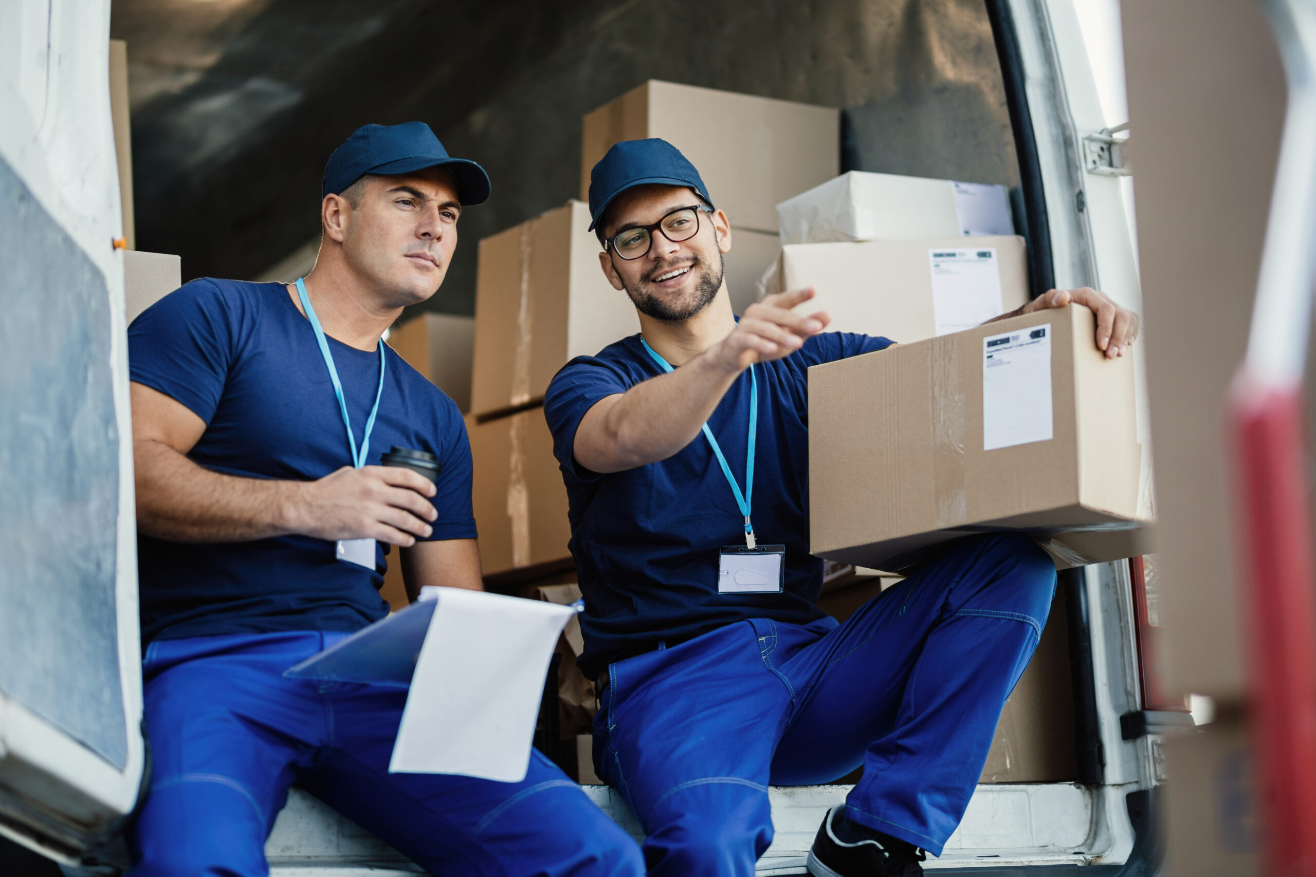 young courier pointing something while witting with his coworker back delivery van scaled